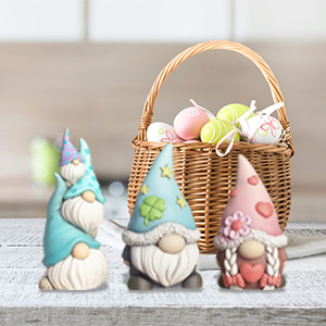 Weidenkorb mit pastellfarbenen Eiern neben drei dekorativen Zwergenfiguren in pastellfarbenen Outfits. Zwerge haben markante