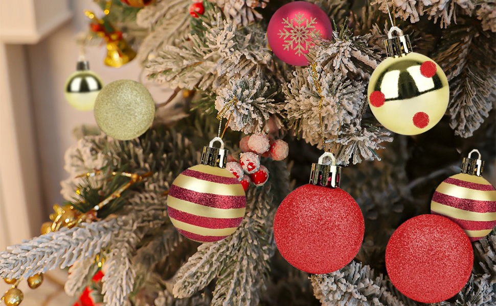 Nahaufnahme der Weihnachtsbaumzweige mit Ornamenten. Rote, goldene und weiße Kugeln hängen an Tannenzapfen, die mit Schnee bedeckt sind.