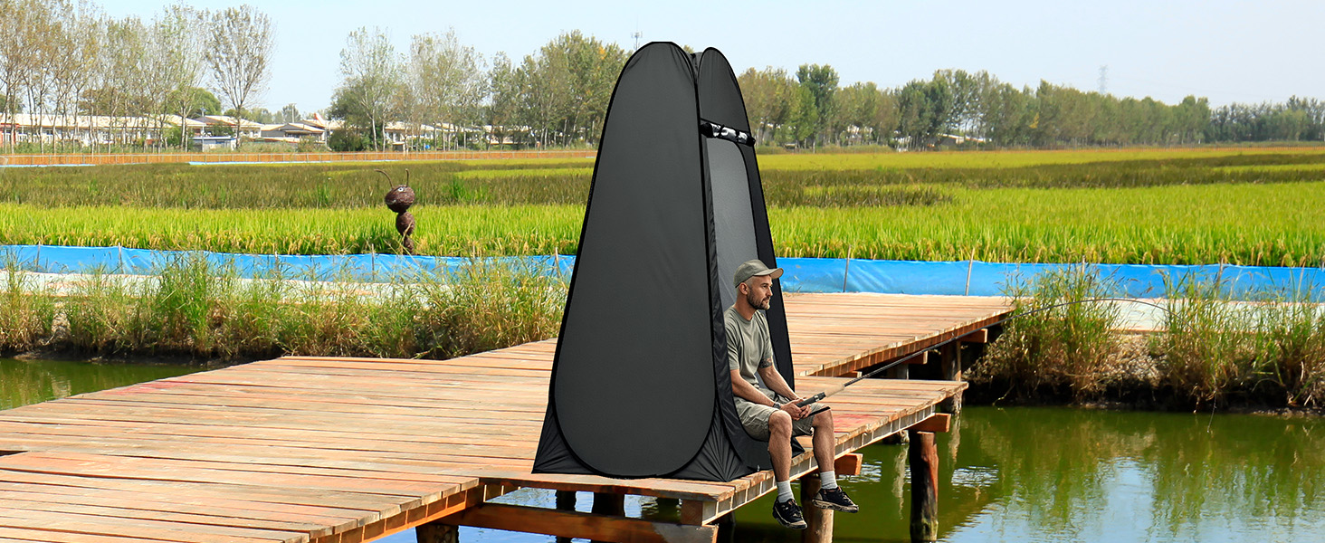 installée sur un quai en bois au-dessus de l'eau. Structure noire en forme de dôme avec une personne partiellement visible à l'intérieur. Paysage herbeux environnant et arbres visibles.