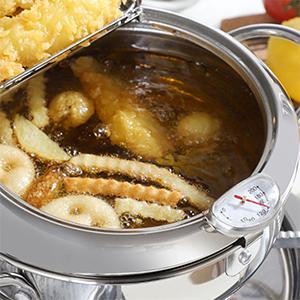 Pentola in acciaio inossidabile con olio bollente, contenente cibi impanati che vengono fritti. Pasta o tagliatelle visibili sul lato.