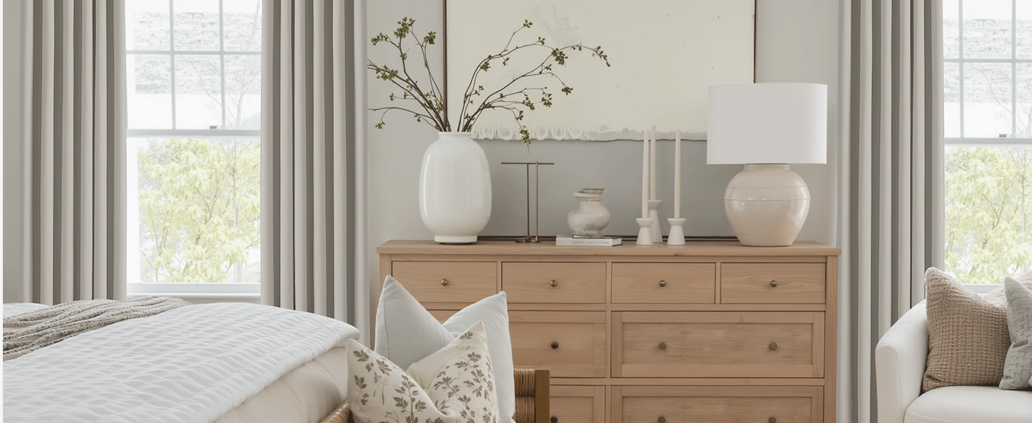 Bright living room interior with natural wood chest of drawers, white curtains and decorative vases. Large windows provide natural light. The interior of the modern living room includes a beige corner sofa, gray curtains, and large windows with natural light. Width=