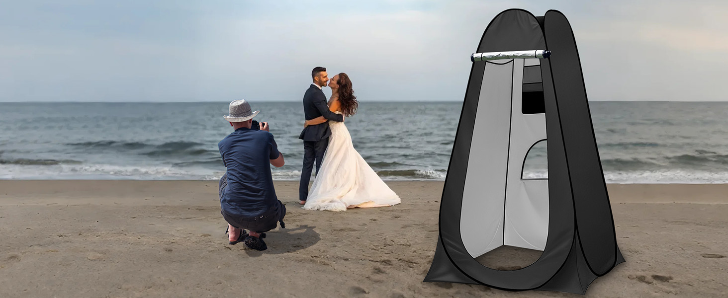 Tente d'intimité escamotable noire sur une plage. Vestiaire portable avec porte zippée. L'océan et le rivage sablonneux sont visibles en arrière-plan.