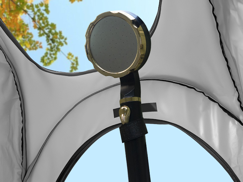 Miroir circulaire cerclé doré attaché à une sangle noire à l'intérieur d'une tente. Le miroir reflète le ciel bleu et le feuillage vert. Deux fenêtres de tente visibles en arrière-plan.