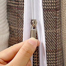 Gros plan d'une main tirant sur une fermeture éclair blanche attachée à un tissu beige, contrastant avec un fond texturé plus foncé