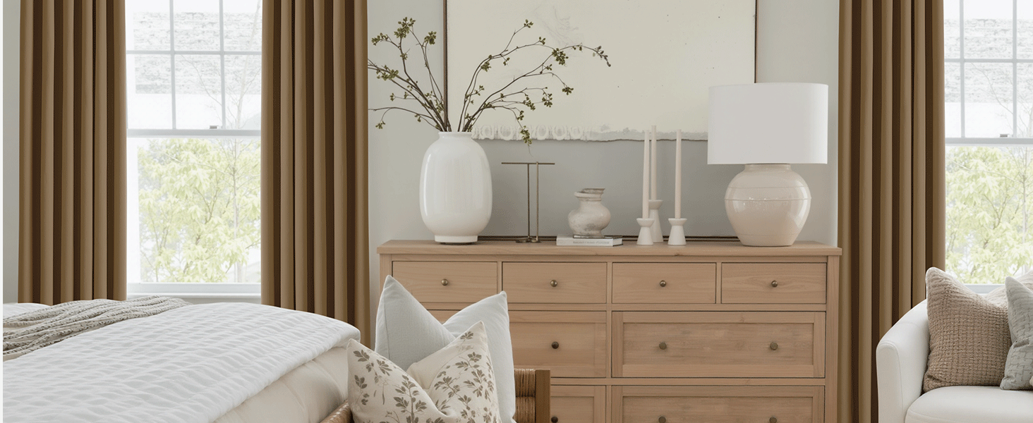 Intérieur lumineux du salon avec commode en bois naturel, rideaux blancs et vases décoratifs. Les grandes fenêtres fournissent un éclairage naturel.