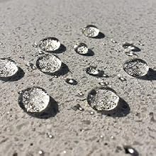 Photographie rapprochée de gouttelettes d'eau sur une surface de béton gris, démontrant des propriétés hydrofuges ou hydrophobes
