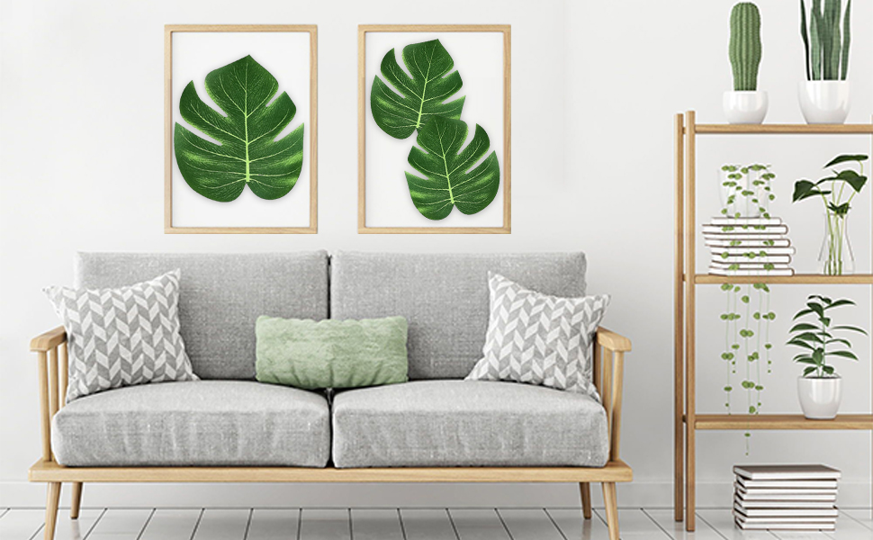 Intérieur du salon avec canapé gris, coussin vert, imprimés de feuilles de monstera encadrés et décor végétal. Design moderne d'inspiration scandinave