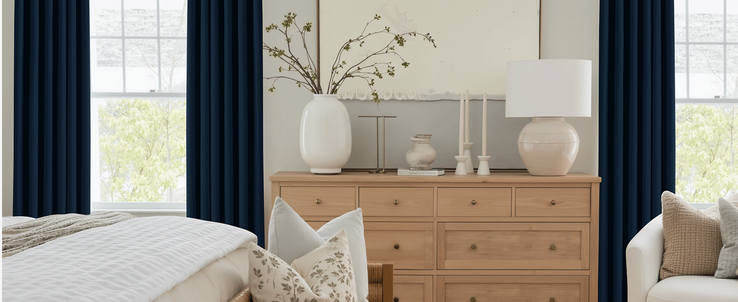 Bright living room interior with natural wood chest of drawers, white curtains and decorative vases. Large windows provide natural light. The interior of the modern living room includes a beige corner sofa, gray curtains, and large windows that let in plenty of daylight. data-orig-src=