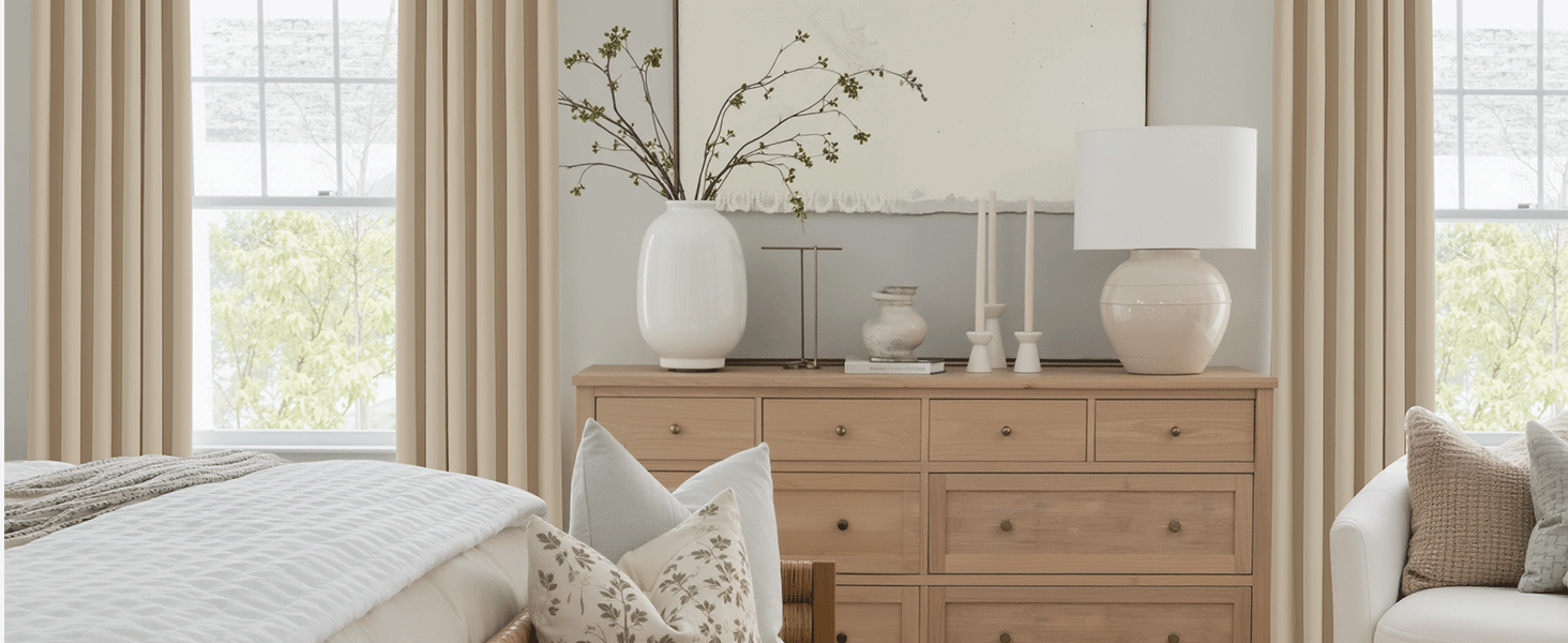 Intérieur lumineux du salon avec commode en bois naturel, rideaux blancs et vases décoratifs. Les grandes fenêtres fournissent un éclairage naturel.