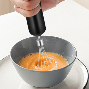 Appareil portable noir distribuant un liquide orange dans une casserole grise ou un récipient de cuisson sur fond blanc.