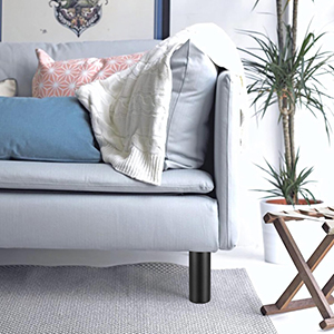 Canapé gris avec oreillers et couverture, plante en pot sur support en bois, décor intérieur lumineux