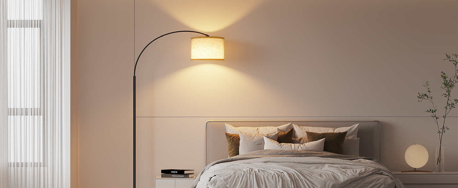 Modernes Schlafzimmer mit gewölbter Stehlampe mit cremefarbenem Stoffschirm, der warmes Licht auf das graue Polsterbett mit neutraler Bettwäsche und dekorativen Kissen wirft