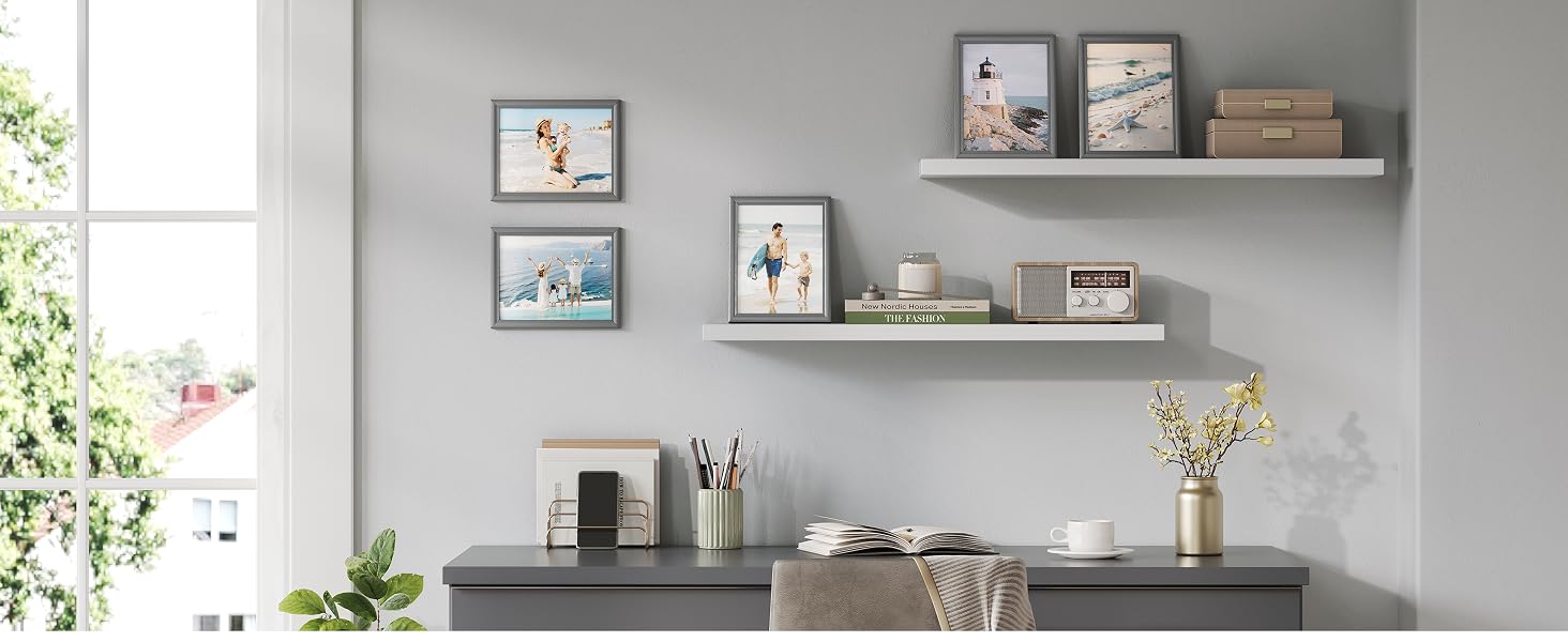Sistema di scaffali grigi a parete con stampe botaniche incorniciate, contenitori in ceramica bianca contenenti articoli per l'arte, vaso di vetro con fiori secchi e piante in vaso sulla scrivania.