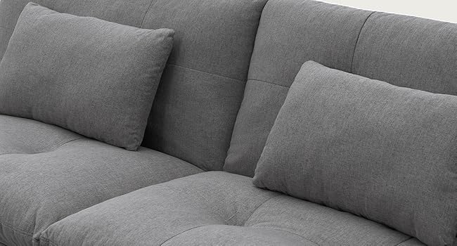 Sofá o sofá tapizado en gris con varios cojines y almohadas dispuestos sobre un fondo neutro, que exhibe muebles textiles para sentarse en el contexto de la sala de estar.