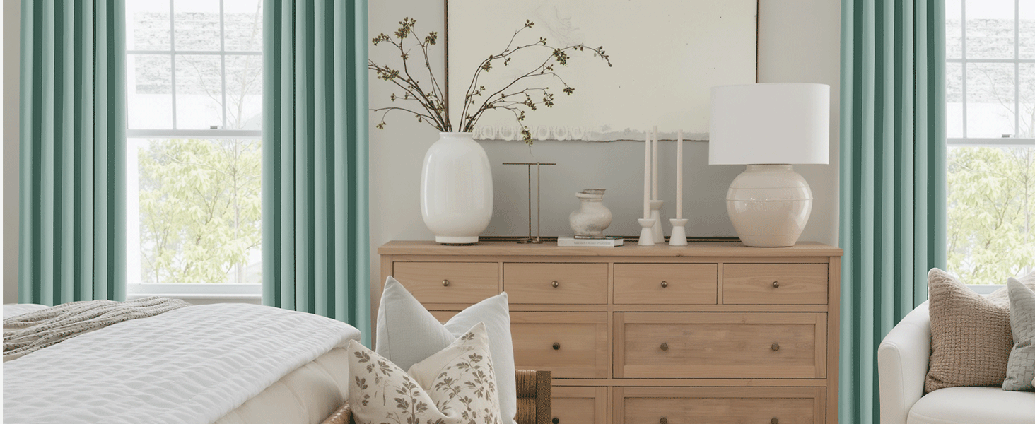 Sala de estar luminosa con cómoda de madera natural, cortinas blancas y jarrones decorativos. Grandes ventanales que proporcionan luz natural.