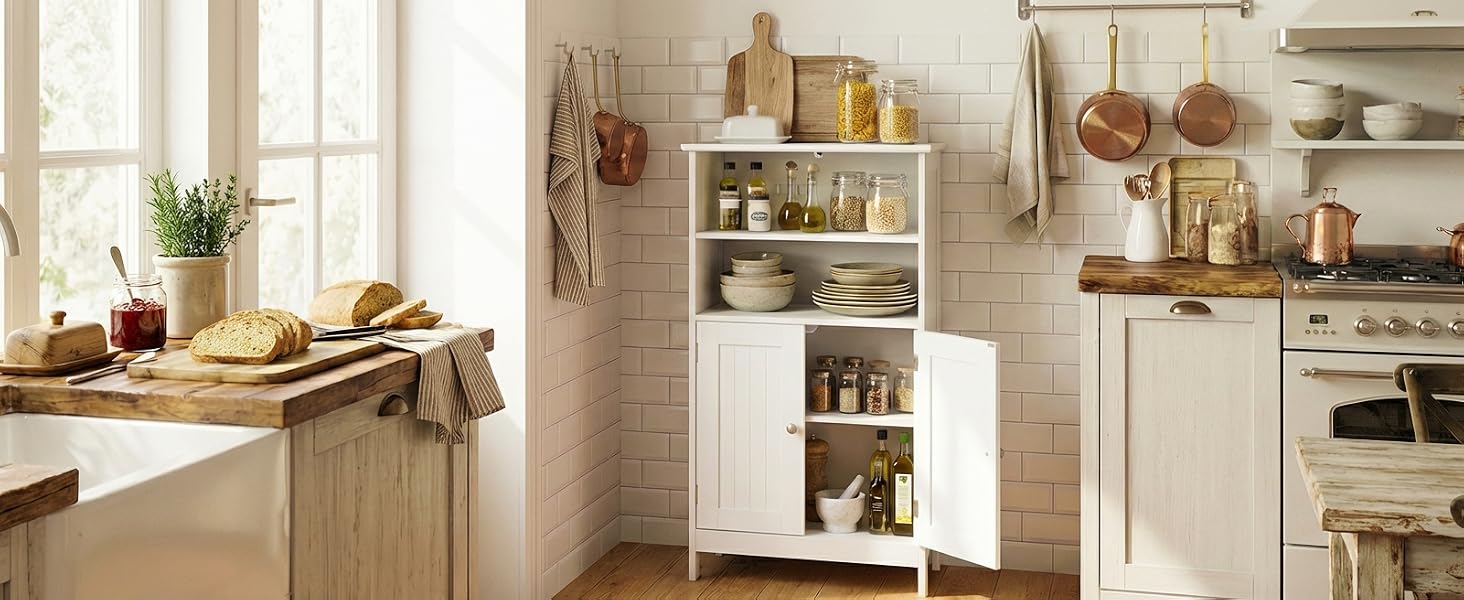 L'intérieur de la cuisine rustique comprend des murs en carreaux de métro blancs, des comptoirs en bois et des étagères ouvertes présentant des ustensiles de cuisine en cuivre, des plats en céramique et divers accessoires de cuisine dans une palette de couleurs chaudes et neutres.