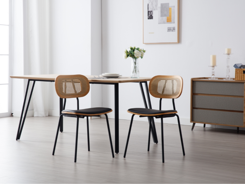 Moderne Essgruppe mit rechteckigem Holztisch, schwarzen Metallbeinen und zwei Stühlen mit Rattanlehne. Graues Sideboard und weißer Blumentafelaufsatz runden die minimalistische Raumgestaltung ab