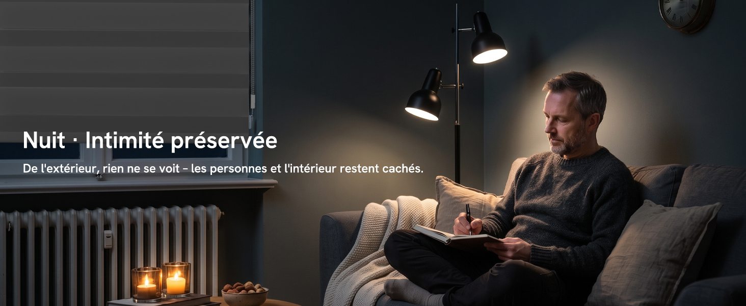 Le texte se lit comme suit : « Nuit • Intimité préservée. De l'extérieur, rien ne se voit — les personnes et l'intérieur restent cachés. » Homme lisant sur un canapé la nuit avec lampe allumée, stores pour plus d'intimité.