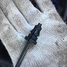 Small black plastic component with a thin metal rod protruding from one end, resting on a light-colored knit fabric surface.