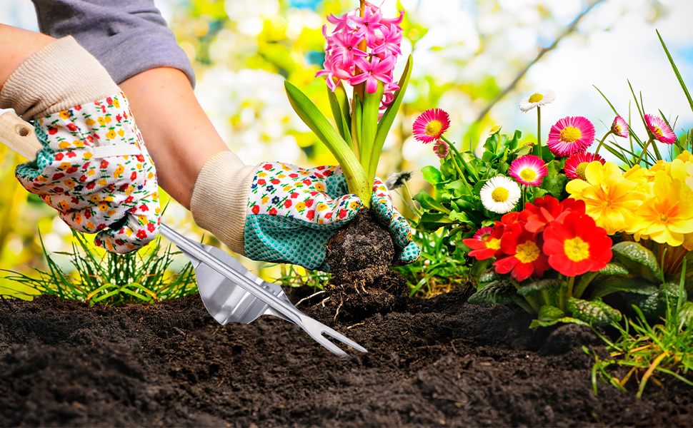 Hands wearing colorful patterned gardening gloves using a small trowel to plant vibrant flowers in soil, surrounded by various blooming plants.