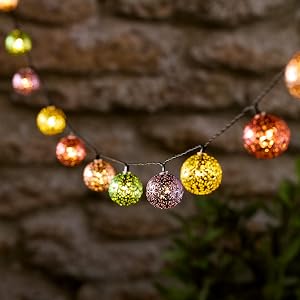 String of colorful, glittery ball-shaped lights against a rustic stone background. Lights in yellow, orange, green, and purple hues.
