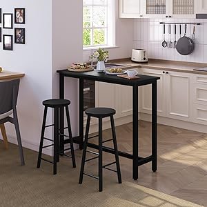 Cucina moderna con armadi bianchi, con un tavolo nero alto da bar e due sgabelli abbinati. Gli utensili sono appesi al muro, l'arte incorniciata è visibile