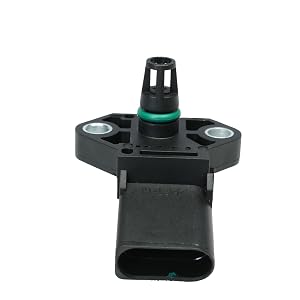 Close-up of a black plastic automotive sensor or component with a green ring and electrical connector. Mounted on a flat surface.