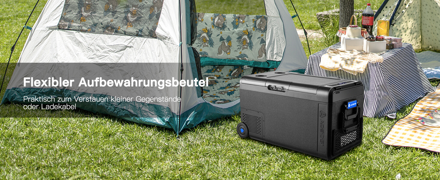 Tragbarer Aufbewahrungsbehälter mit flexibler Aufbewahrungstasche, ausgestellt auf Gras im Freien. Schwarzes elektronisches Gerät und Camping-/Outdoor-Setup im Hintergrund sichtbar