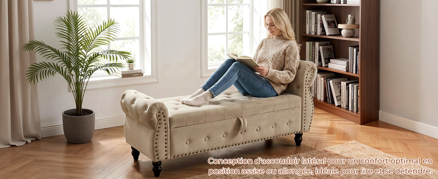 Femme en cardigan beige et jean lisant sur un fauteuil à ailes rembourré crème dans un salon lumineux avec plante en pot et étagère visibles.