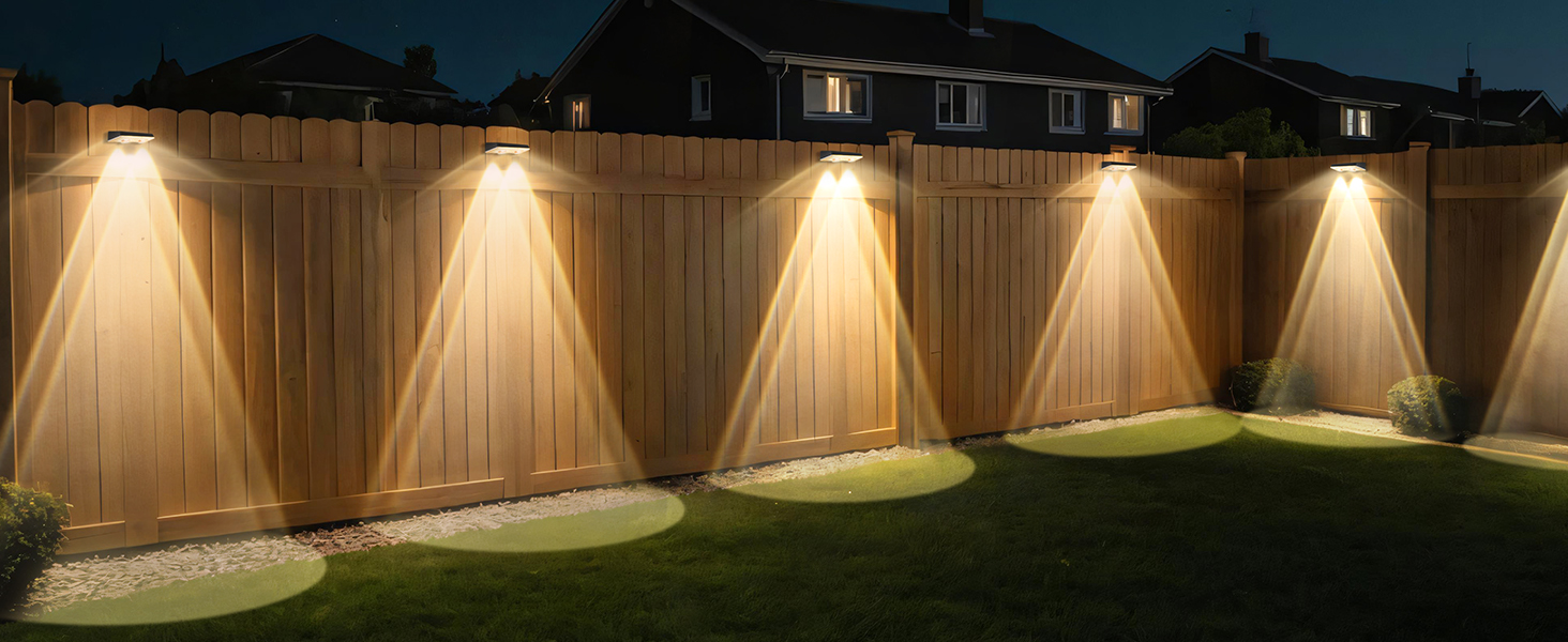 Lampes solaires extérieures montées sur des panneaux de clôture en bois, illuminant une cour arrière la nuit. Chaque lampe projette un faisceau triangulaire chaud sur l'herbe située en dessous.