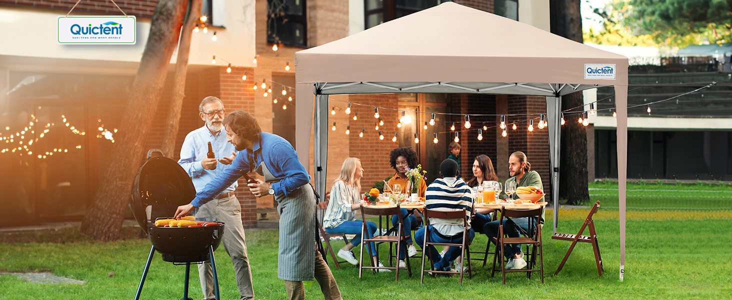 Rassemblement en plein air avec des personnes autour d'une table sous un auvent blanc. Grille au premier plan, guirlandes lumineuses visibles. Le logo indique « Quictent » sur
