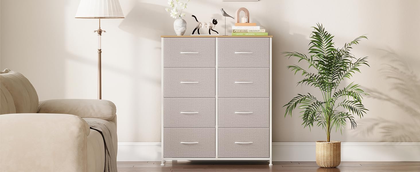 avec 8 tiroirs gris clair. Cadre et plateau en bois blanc. Situé dans un salon avec une plante et une lampe à proximité.