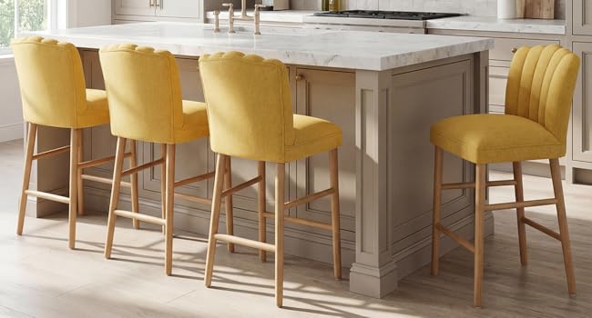 Îlot de cuisine moderne avec plan de travail gris clair, quatre tabourets de comptoir rembourrés jaune moutarde avec pieds en bois, armoires blanches visibles en arrière-plan.
