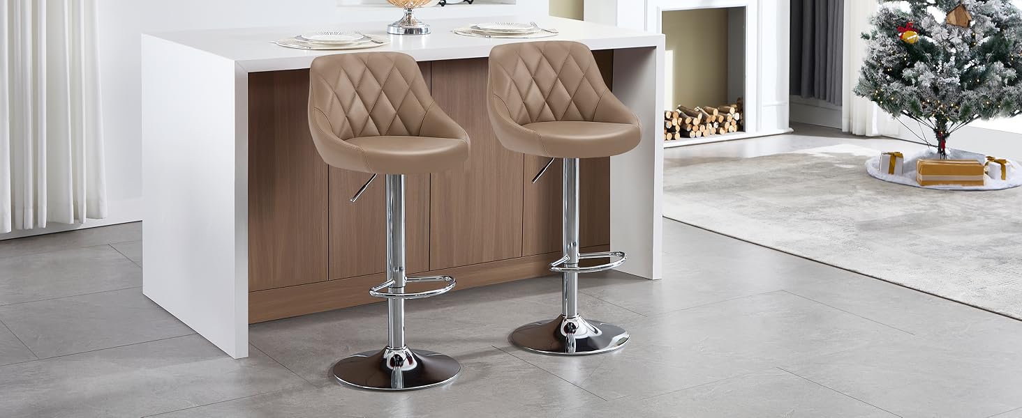 Dos taburetes de bar acolchados de color beige con altura ajustable y bases cromadas, colocados en una isla de cocina blanca. Árbol de Navidad visible en segundo plano