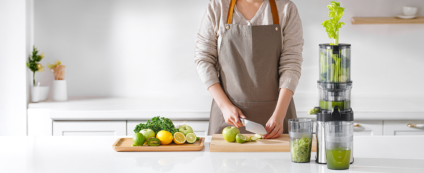 Scène de cuisine avec une personne préparant des fruits et des légumes. Le comptoir affiche une planche à découper, des fruits et légumes et un presse-agrumes ou un mixeur électrique contenant du liquide vert