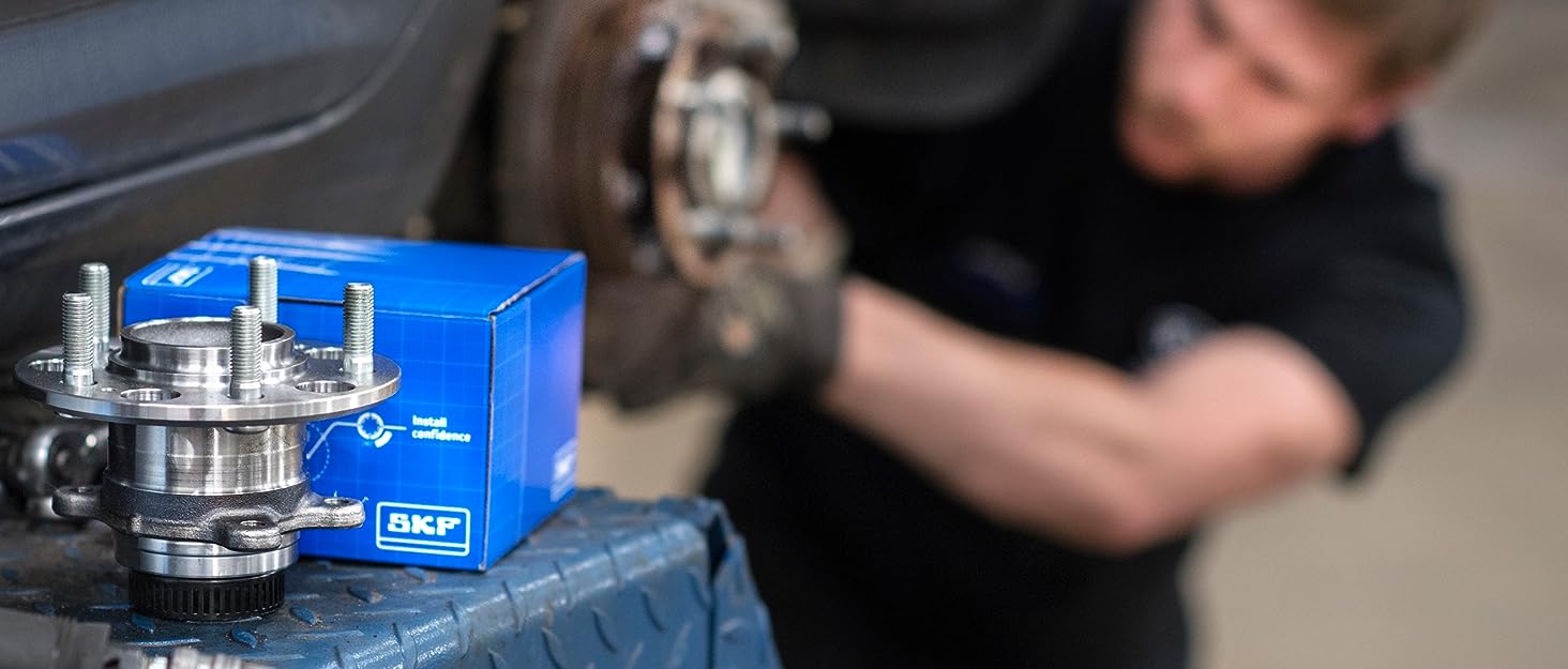 Blue boxed SKF brand wheel bearing or automotive part. Mechanic working on vehicle in background, suggesting installation context.
