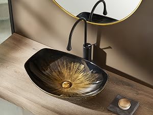 Lavabo artístico de baño con cuenco ovalado negro y patrón de rayos solares dorados. Grifo negro y espejo redondo con borde dorado sobre encimera de madera.