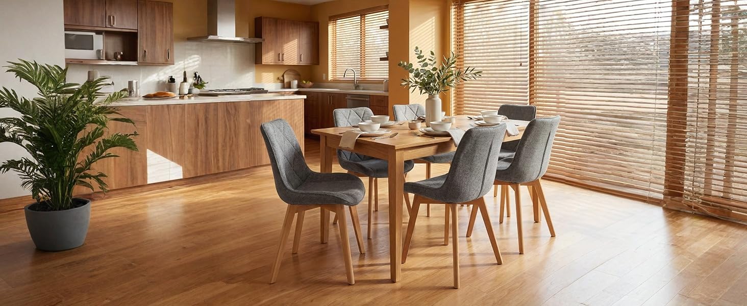 L'intérieur de la salle à manger comprend une table en bois avec quatre chaises rembourrées, des plantes en pot et de grandes fenêtres avec des stores à rayures donnant sur le paysage naturel.