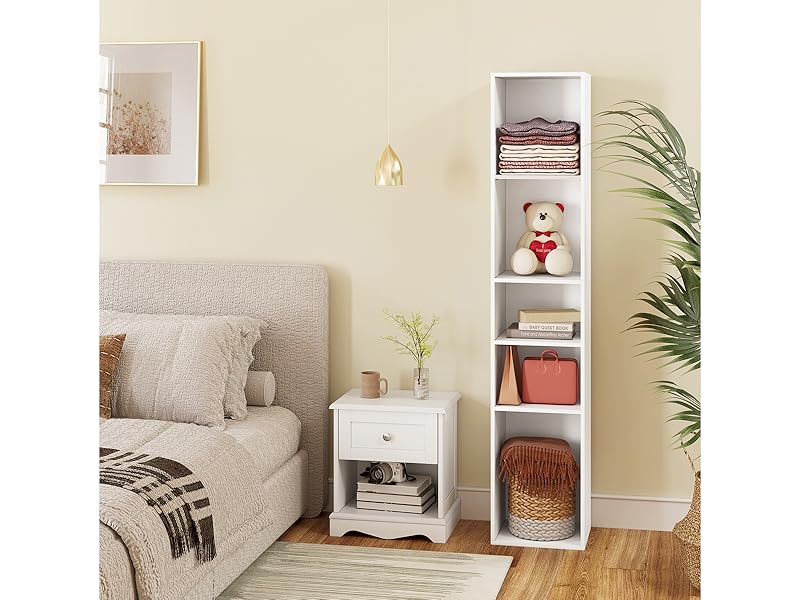 Living room corner with beige sofa, white side table, tall white shelving unit, and decorative items. Neutral color scheme with plant accents.