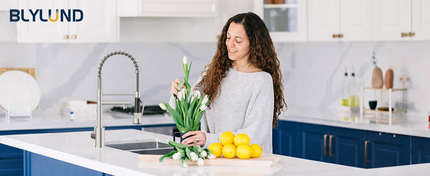 Modern kitchen faucet in use. Stainless steel finish with high arc spout. Person washing lemons, showcasing faucet's functionality in kitchen setting.