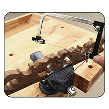Primer plano de una pinza de carpintería que asegura una pieza de madera a una mesa de trabajo. En el fondo se ve una herramienta manual