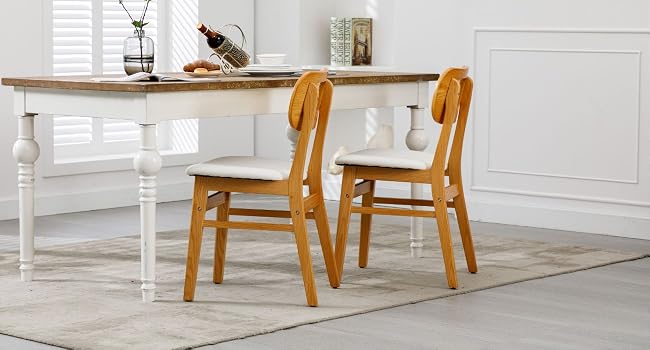 con mesa de madera con patas blancas y tapa de madera natural. Dos sillas de madera a juego con asientos acolchados de color crema complementan