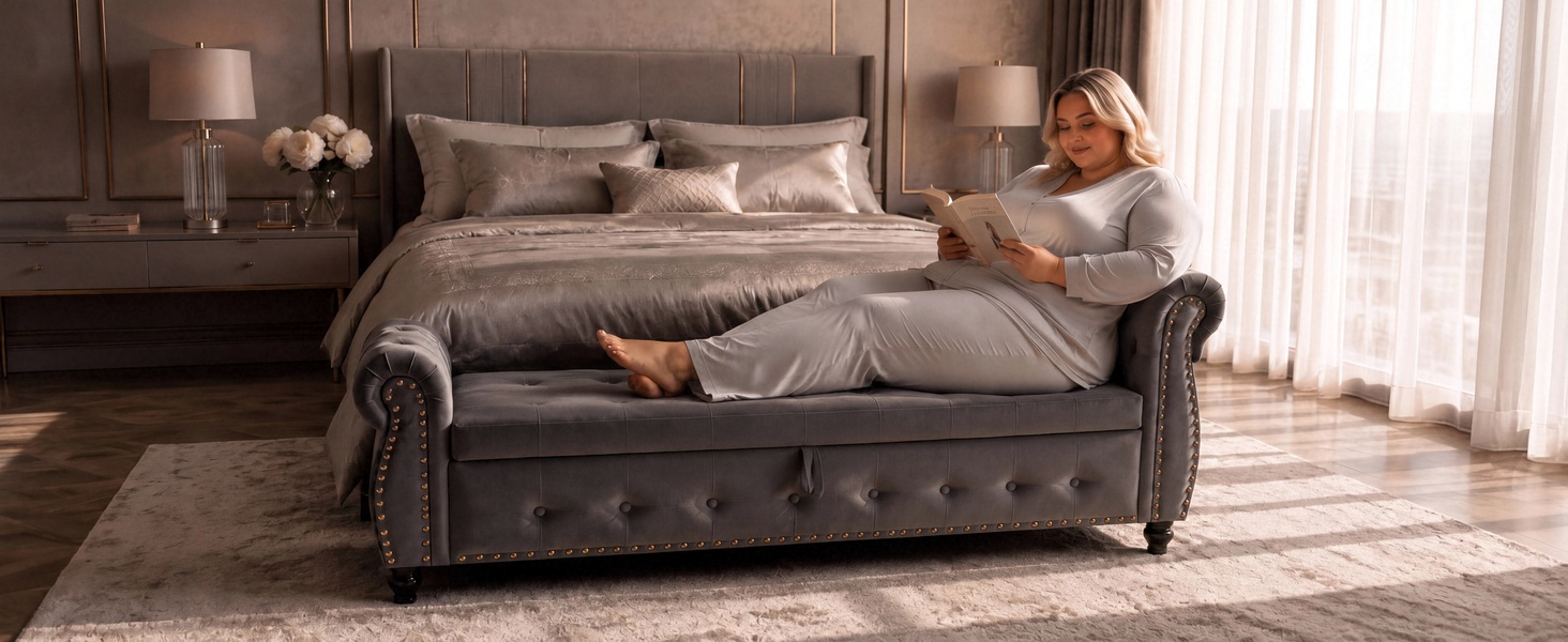 Gray upholstered sofa with rolled arms in residential living room with white curtains and wooden flooring visible.