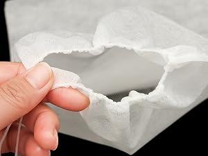 Doigts tenant un matériau doux, blanc et flexible avec un bord déchiré. Le matériau semble léger et poreux, il peut s'agir d'un type de mousse ou de rembourrage.