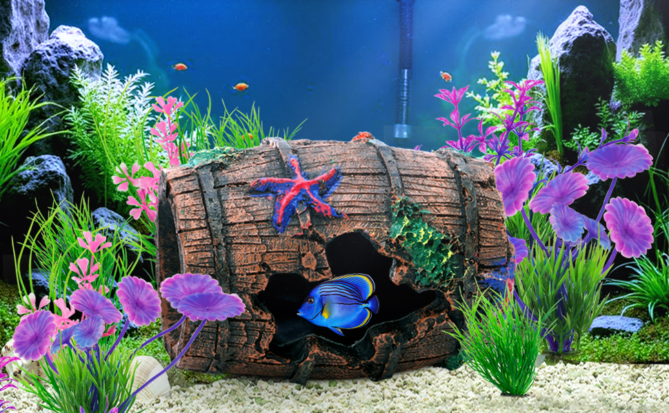 Aquarium display with decorative wooden barrel structure, vibrant purple flowers, and blue tropical fish swimming among lush aquatic plants against light background.