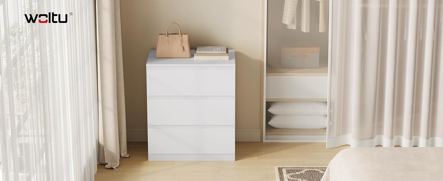 Testo visibile: 'WAKU'. Cassettiera o mobiletto bianco minimalista addossato a una parete bianca con tende, decorato con accessori neutri e asciugamani sulla parte superiore.