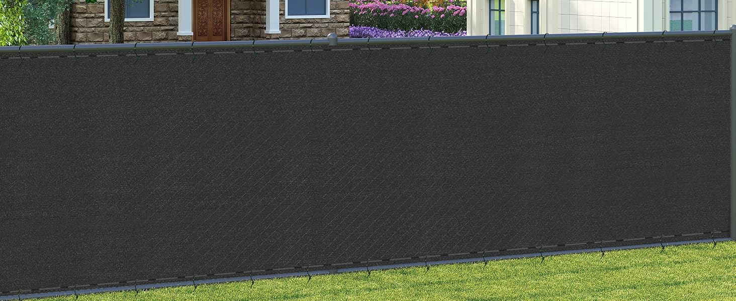 Recinzione o schermo per la privacy grigio scuro installato lungo un prato, con edifici visibili sullo sfondo. Progettato per uso esterno in ambienti residenziali.