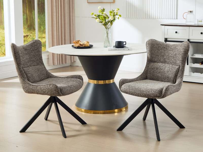 Modern dining set featuring round white table with black and gold base, paired with two gray upholstered swivel chairs in bright interior setting.