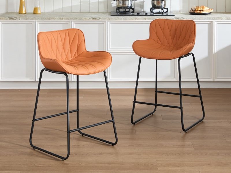 Due moderni sgabelli da bar con rivestimento trapuntato in similpelle cognac e basi a slitta in metallo nero, esposti in un ambiente da cucina con piano di lavoro in legno.