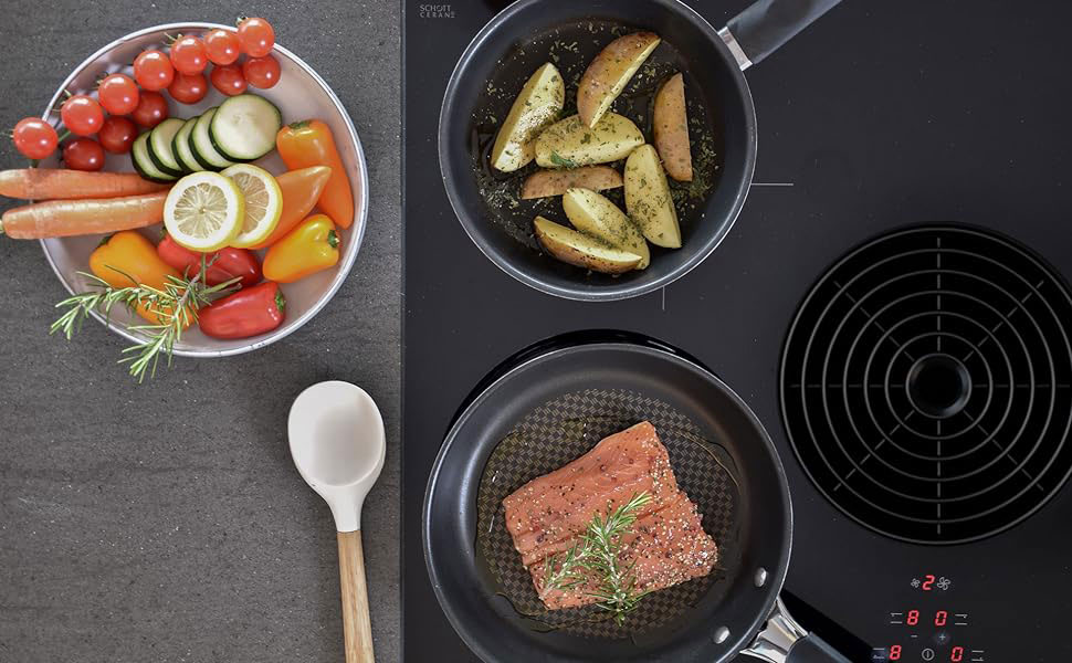 Table de cuisson à induction avec trois poêles : une contenant des légumes frais, une autre avec des pommes de terre rôties et une troisième avec un bifteck cru. Une cuillère en bois est visible.
